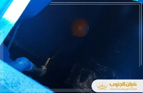 صيانة الخزانات بأبها 0530609402 كيان الجنوب لقطة داخلية لخزان مياه معزول باللون الداكن، تُظهر عوامة برتقالية وأنبوب مياه.